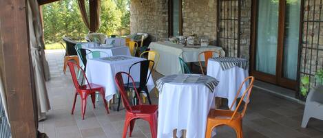 An outdoor dining area with multiple tables and chairs, stone walls, and large windows.