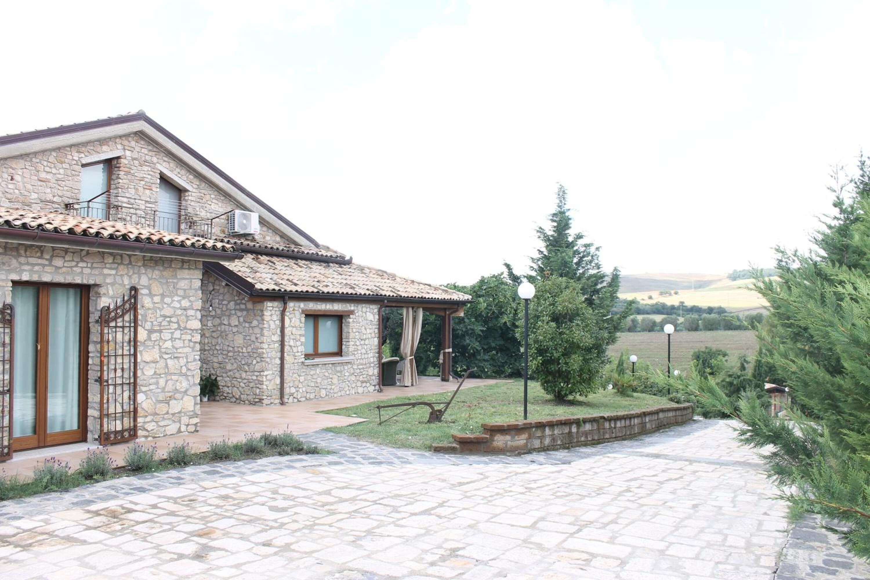 Una casa de piedra con techo de tejas, un porche cubierto y un camino de entrada pavimentado.