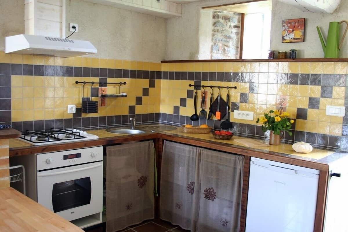 Een kleine keuken met een gasfornuis, oven, spoelbak en een kleine koelkast.