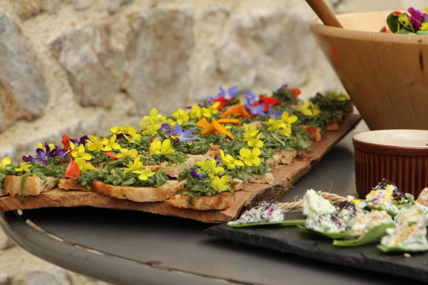 A wooden board with various food items, including a salad and a dish with colorful flowers.