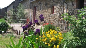 A stone building with multiple windows and a garden with purple and yellow flowers. - Aux Bonnes Herbes (Bais)