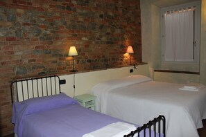Una habitación con dos camas, una pared de piedra y un ventanal con cortinas.