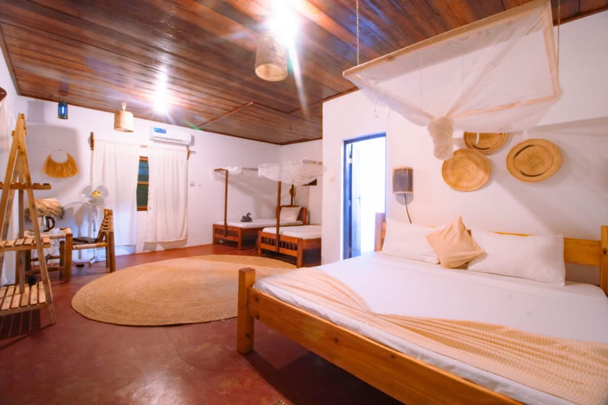Una habitación con una cama de madera, un tapete redondo tejido, una silla de madera, una mesita y un ventilador de techo.