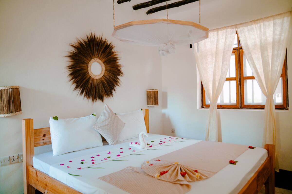 Una cama con sábanas blancas, un colgador decorativo con diseño de sol y un dosel sobre la ventana.