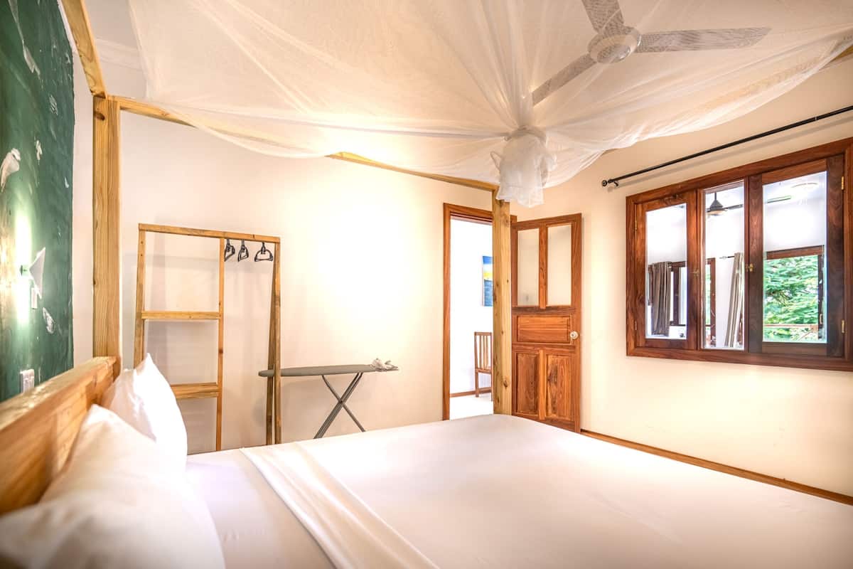 Una habitación con cama, armario de madera, espejo y ventana con cortinas.