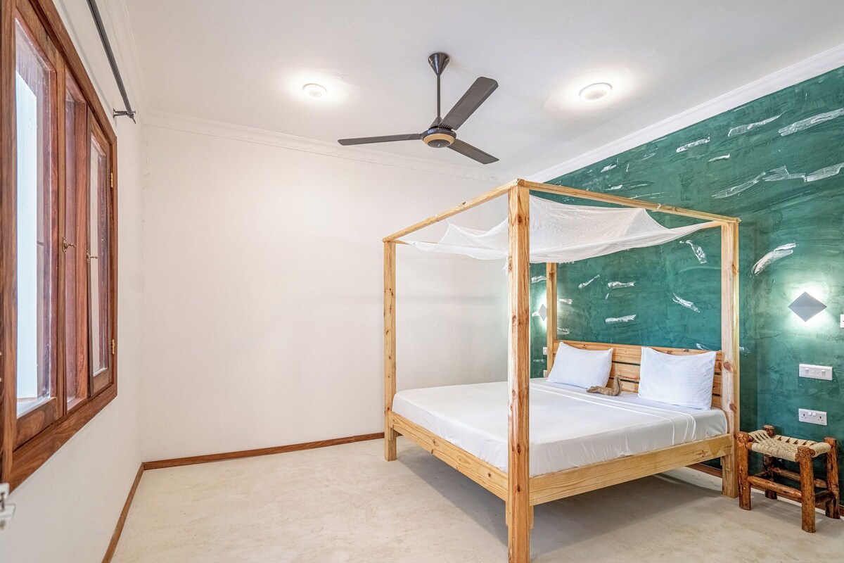 A single bed with a wooden frame and canopy, a ceiling fan, and a green textured wall.