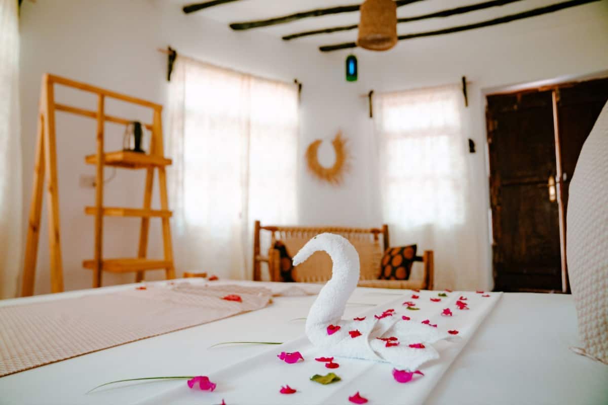Una habitación con una cama, una escalera de madera, un sillón de mimbre y una puerta.