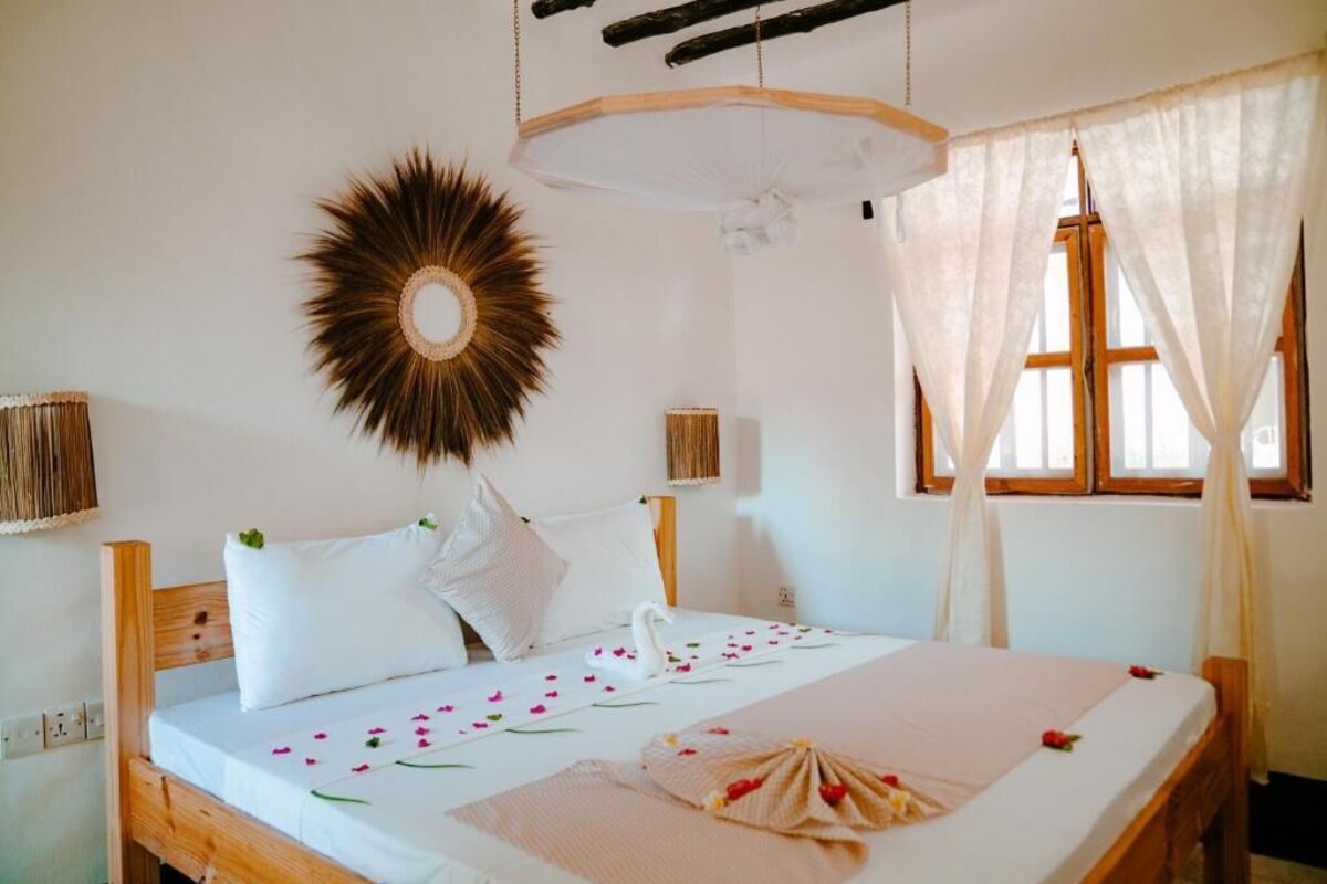 A bed with white linens, a decorative sunburst wall piece, and a swan-shaped pillow.