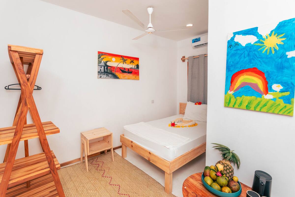 Una habitación con una cama, una escalera de madera, una mesita, un cuadro y un frutero.
