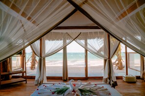 A beach view from a tented room with a bed, a bench, and a small table. - TIKI Beach Club and Resort  (Bwejuu)