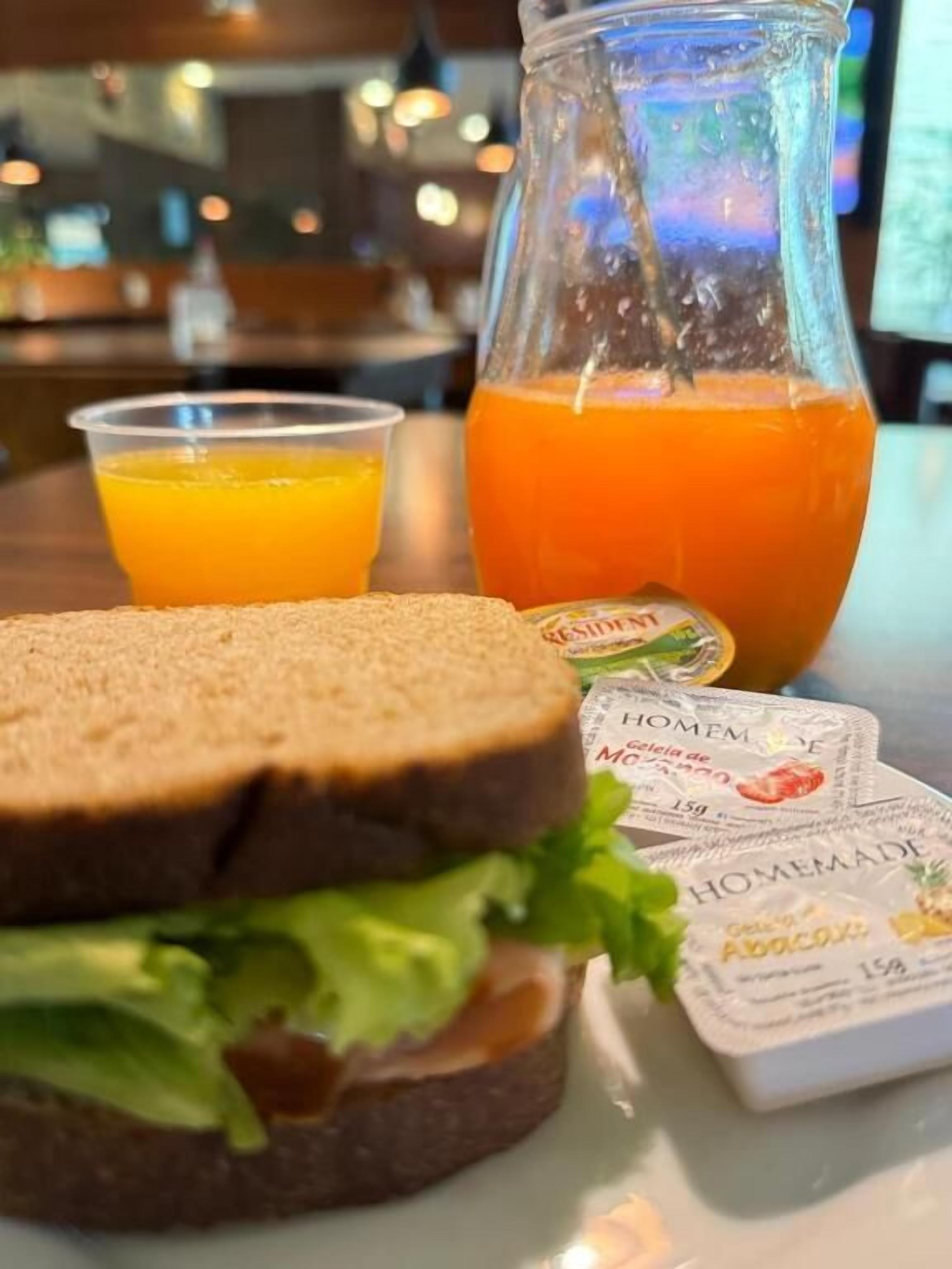 A sandwich with lettuce and a slice of tomato, a glass of orange juice, and a bottle of orange juice on a table.