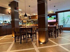A restaurant interior with a central dining area, high wooden pillars, and a large window with a view. - Afford Hoteis (Lages)