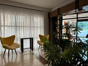 A hotel lobby with two yellow chairs, a black table, and a large window with sheer curtains. - Afford Hoteis (Lages)