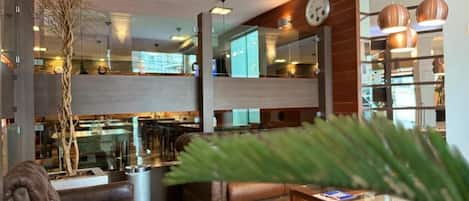 A modern hotel lobby with a seating area, a clock, and a view of the kitchen.
