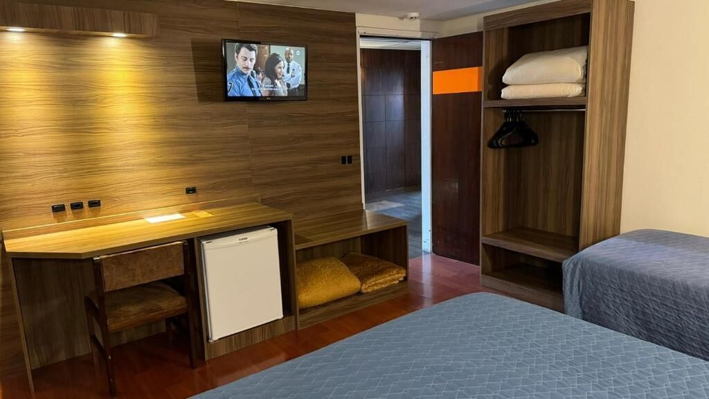 Een hotelkamer met een houten wand, een televisie, een bureau met een minibar, een bed en een kledingkast.