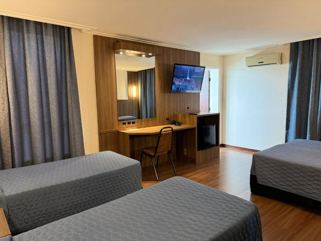 A hotel room with two beds, a desk, a chair, a television, and an air conditioning unit.