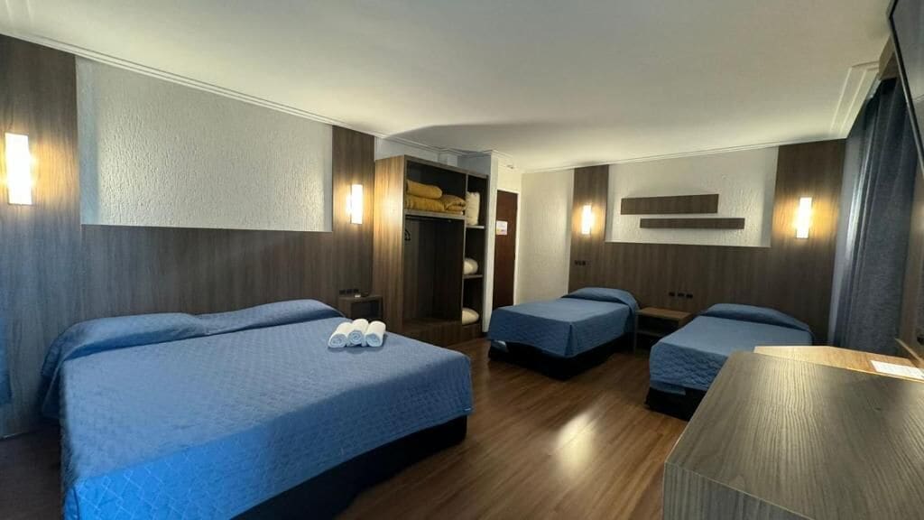 A hotel room with three beds, a wardrobe, and a desk.