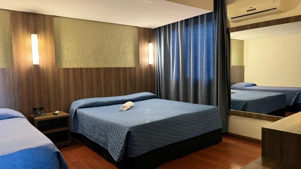Ein Hotelzimmer mit zwei Betten, einem Nachttisch, einem Spiegel und einer Wand-Klimaanlage.