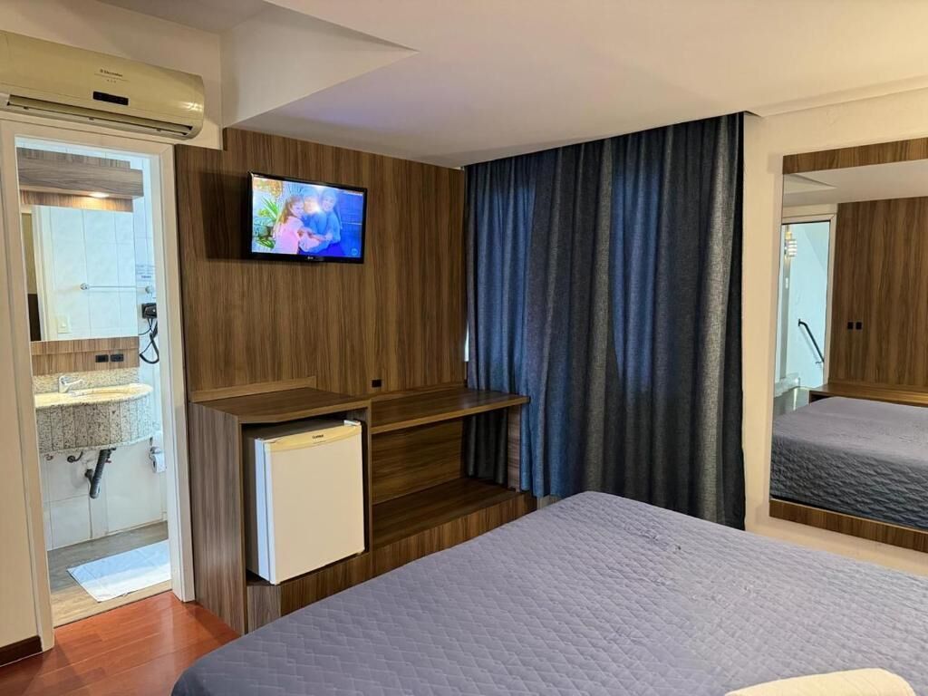 A hotel room with a bed, a television, a small refrigerator, and a bathroom visible through an open door.