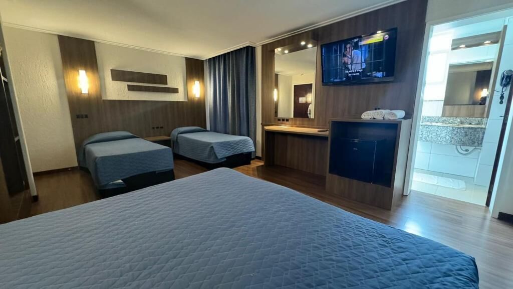 Ein Hotelzimmer mit einem großen Bett, zwei Einzelbetten, einem Schminktisch mit Spiegel, einem Fernseher und einem Badezimmer mit Dusche.