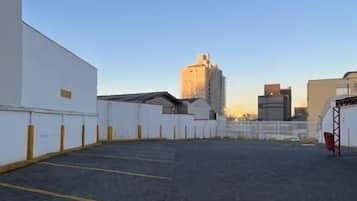 Uma área de estacionamento no terraço, com céu claro, superfície pavimentada e um edifício branco à esquerda.