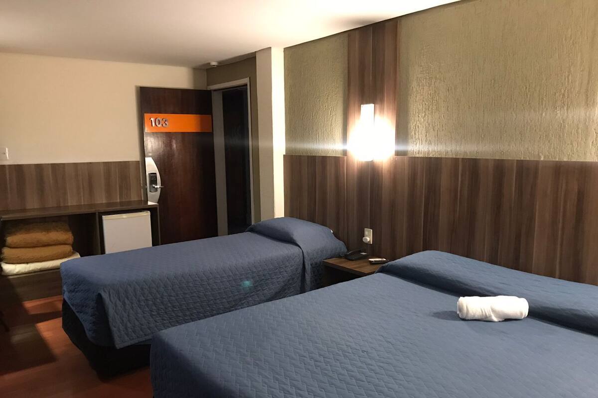A hotel room with two beds, a desk, a mini-fridge, and a bathroom door.
