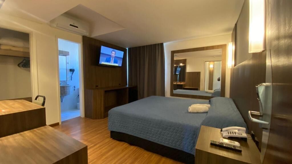 A hotel room with a bed, a TV, a bedside table with a phone, and a mirror.