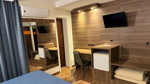 Ein Hotelzimmer mit Bett, Schreibtisch, Stuhl, Fernseher und einer eingebauten Ablage mit Handtüchern.