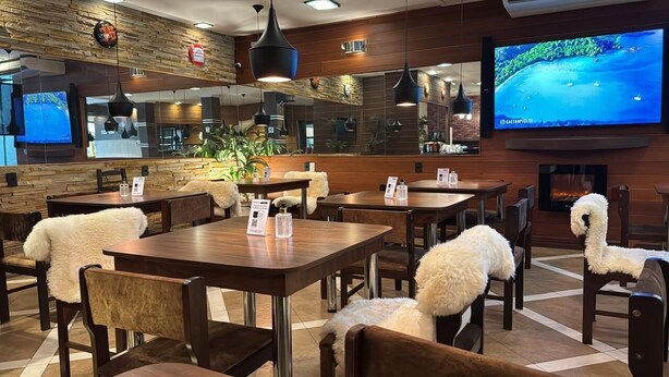 Ein Restaurant mit Holztischen und -stühlen, einem Bildschirm und einem Kamin.