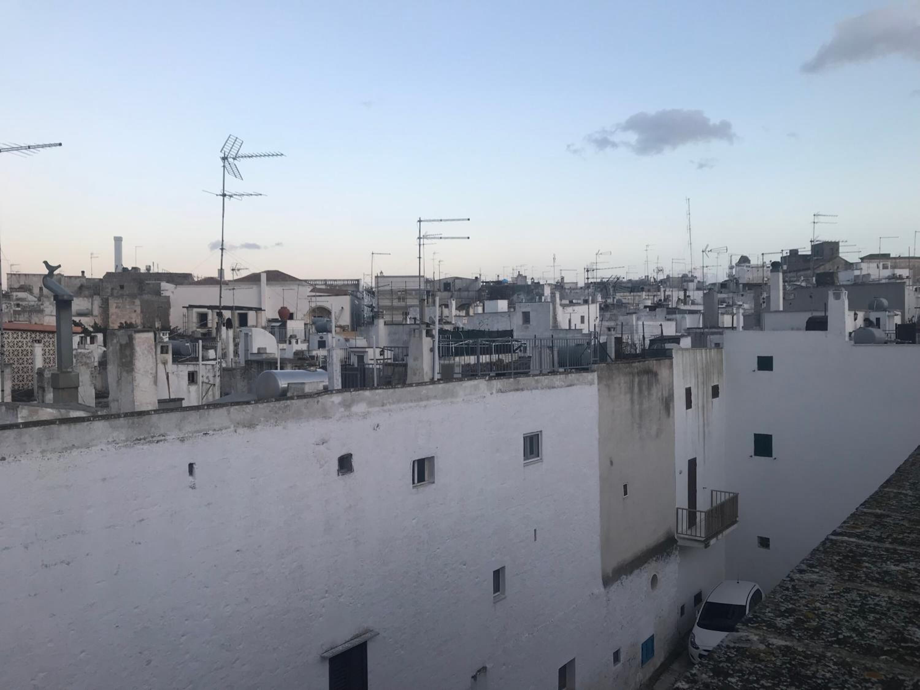 A rooftop with multiple buildings, some with antennas and satellite dishes, and a few vehicles parked.