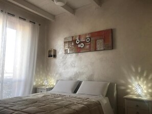 A bedroom with a bed, two bedside tables with lamps, a wall art piece, and a window with curtains. - Bed and Breakfast il Girasole (Ostuni)