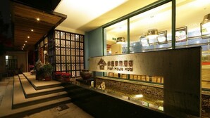 A hotel entrance with a stone pathway leading to the door, a decorative wall with a grid pattern, and a sign indicating the hotel name.
