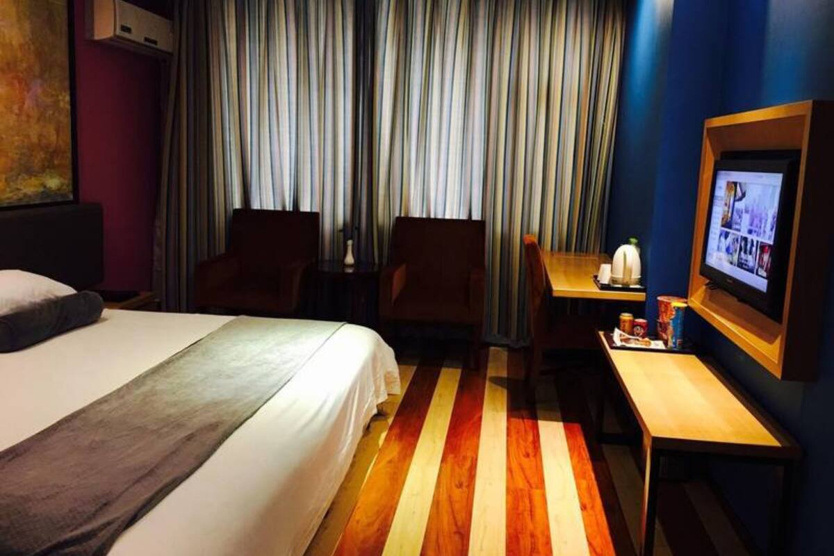 Une chambre d’hôtel avec un lit, deux fauteuils, un bureau avec une télévision et un rideau à rayures.