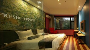 A hotel room with a large bed, a red chair, a small table, and a painting on the wall.