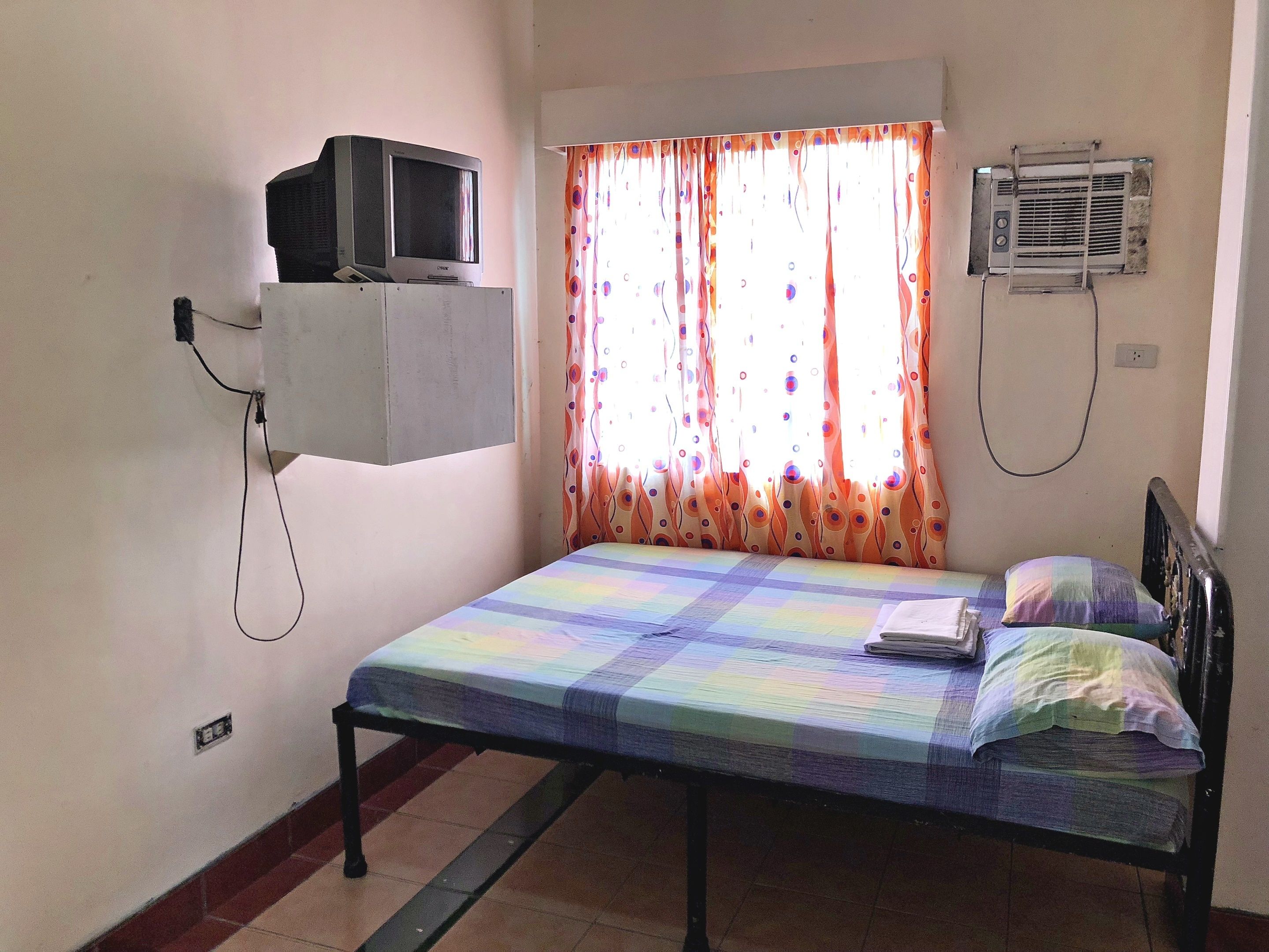 Un dormitorio con una cama, televisión montada en la pared y aire acondicionado.