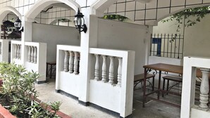 Un espace extérieur abrité, doté de murs blancs, de plusieurs arcades et d’une table en bois.
