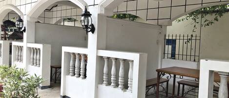 Un espacio exterior cubierto con paredes blancas, varios arcos y una mesa de madera.