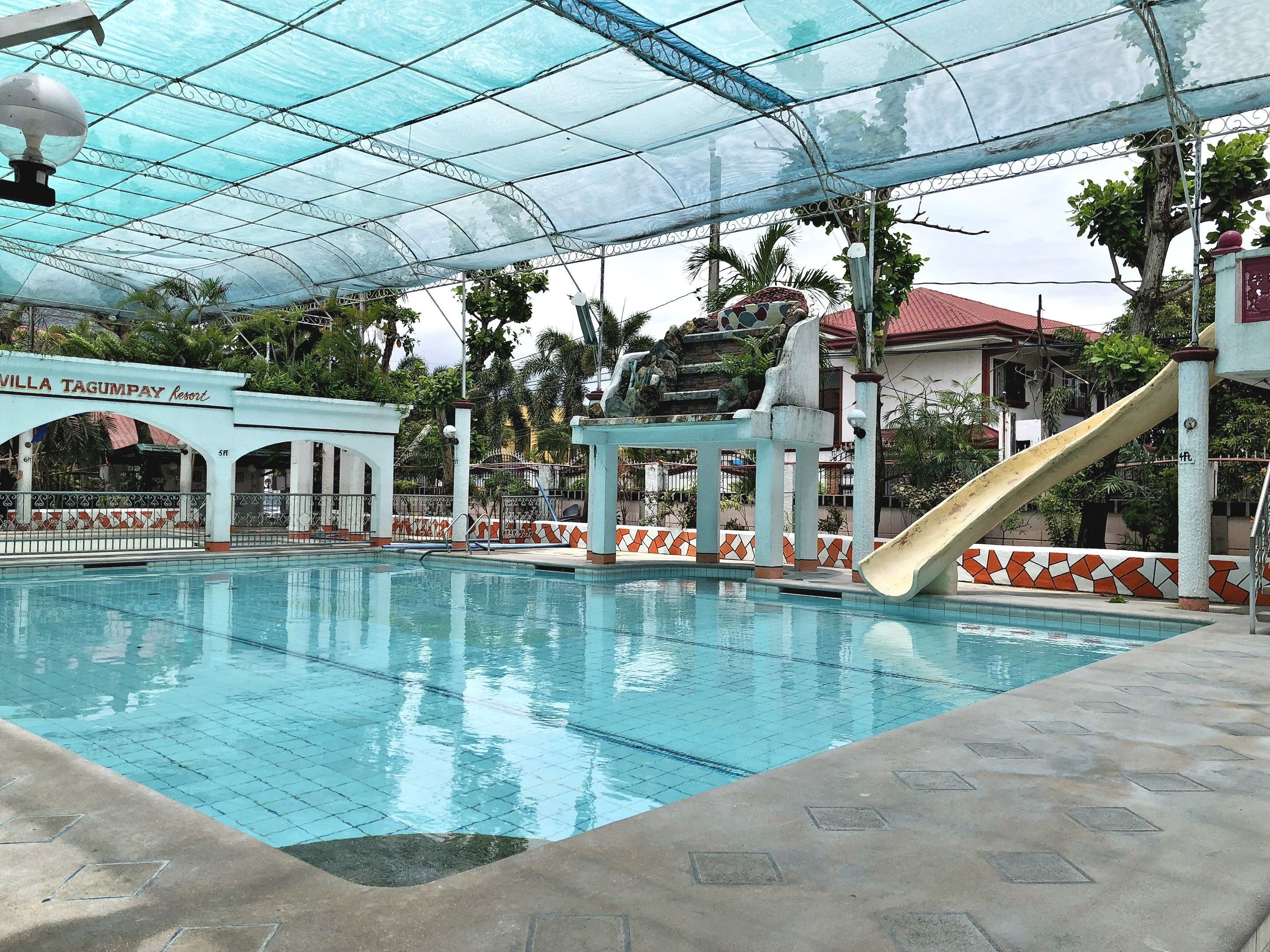 Una piscina con zona cubierta, un tobogán y un edificio que dice 'Villa Tagumpay Resort'.