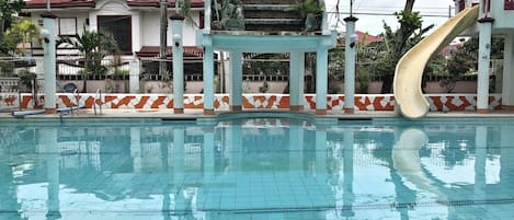 Una piscina con tobogán, rodeada por un patio empinado con baldosas y una cerca decorativa.