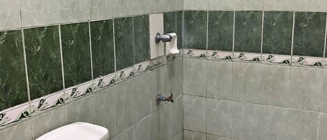 Un baño pequeño con inodoro, un cubo azul y un cabezal de ducha.