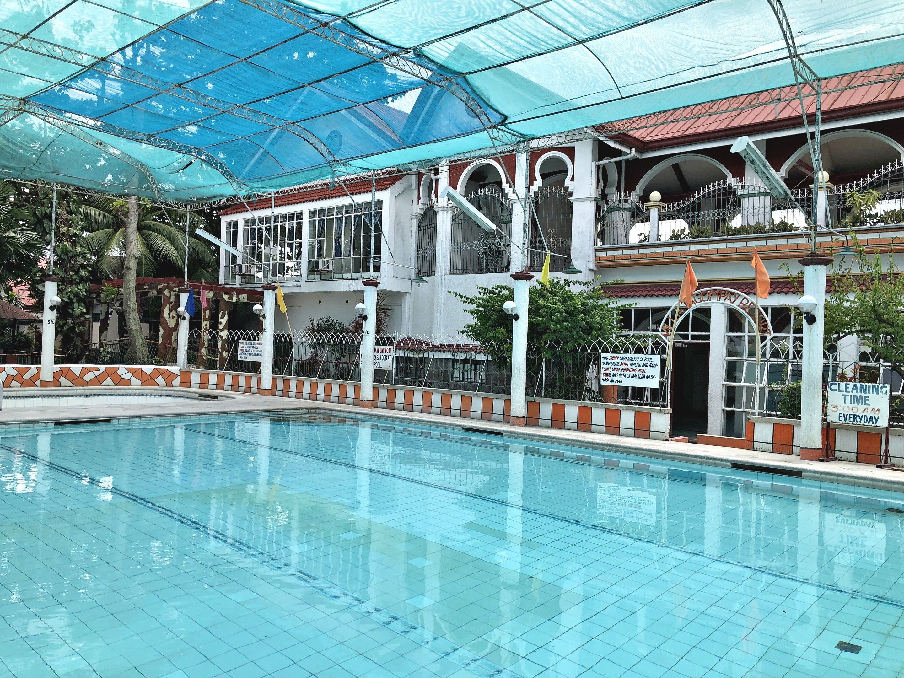A swimming pool with a glass ceiling, surrounded by a building with multiple balconies and a sign indicating cleaning time.