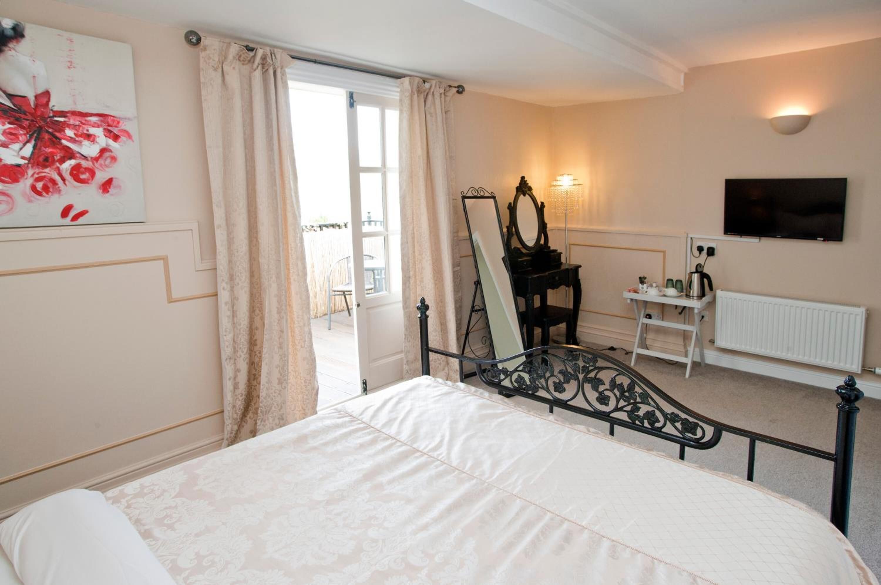 A bedroom with a bed, a dresser, a mirror, a TV, and a window with curtains.