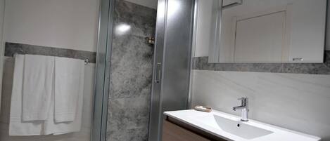Un baño moderno con cabina de ducha de vidrio, un lavabo blanco con mueble de madera y un espejo grande sobre el lavabo.