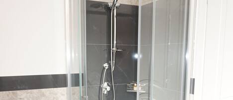 A modern bathroom with a glass-enclosed shower, a white pedestal bidet, and marble flooring.