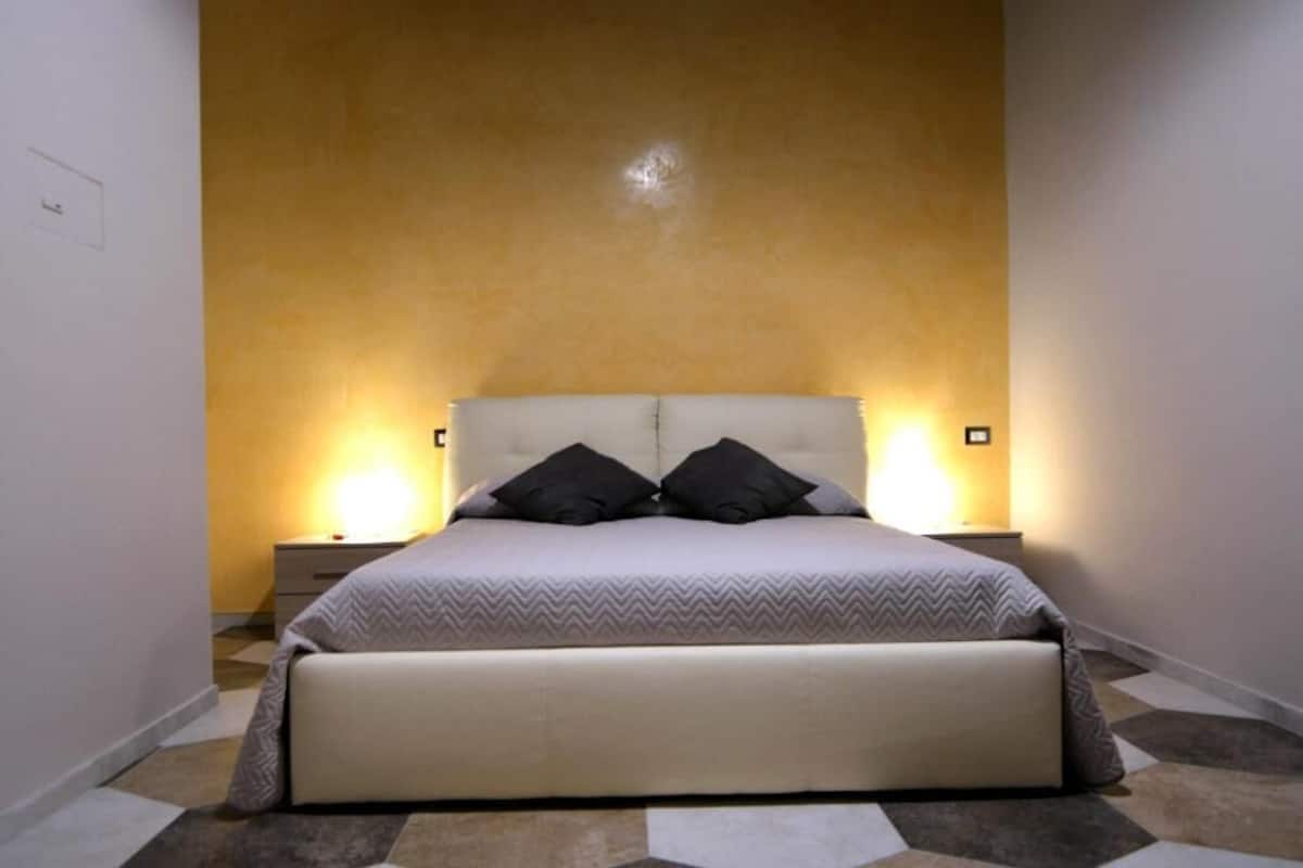 A bedroom with a large bed, two bedside tables, and a wall-mounted light fixture.