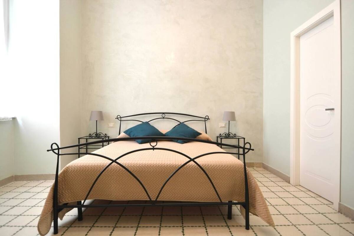 A bed with a metal frame, two bedside tables with lamps, and a plain wall with a door.