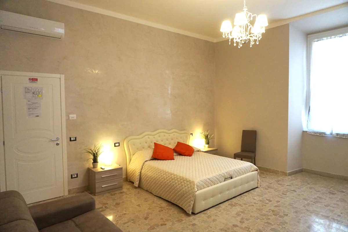 A bedroom with a bed, nightstands, a dresser, a chair, a chandelier, and a door.