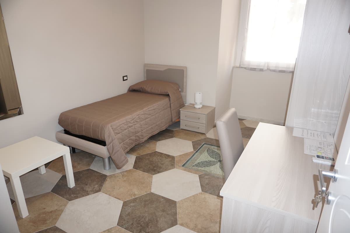 A bedroom with a bed, bedside table, nightstand, and a small desk.