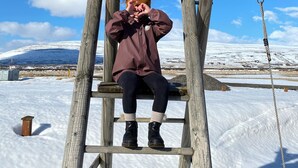 Henkilö istuu puisen tikkaiden päällä lumisessa maisemassa, taivaalla ei ole pilviä.
