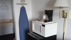 A compact room with a microwave on a small black appliance, a blue ironing board, a lamp, and a wall-mounted ironing board. - Hoosier Inn (Portland)